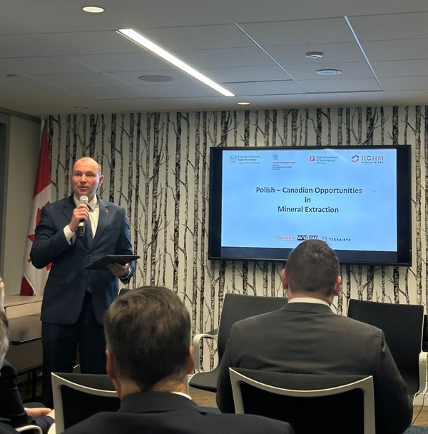 mężczyzna z mikrofonem w ręce podczas prelekcji, na tle ekranu