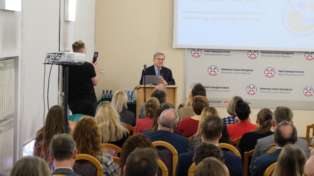 mężczyzna z mikrofonem w ręce podczas prelekcji, na tle ekranu