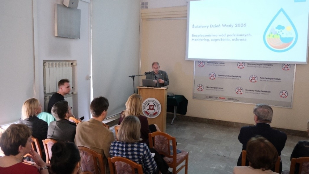 mężczyzna z mikrofonem w ręce podczas prelekcji, na tle ekranu