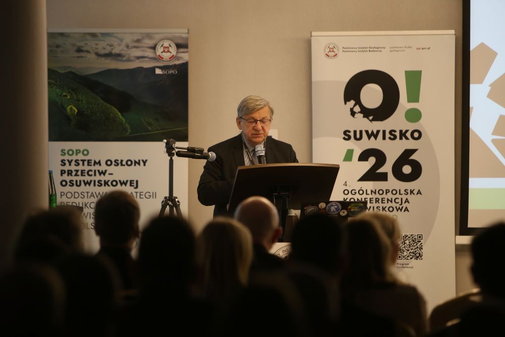 mężczyzna z mikrofonem w ręce podczas prelekcji, na tle ekranu