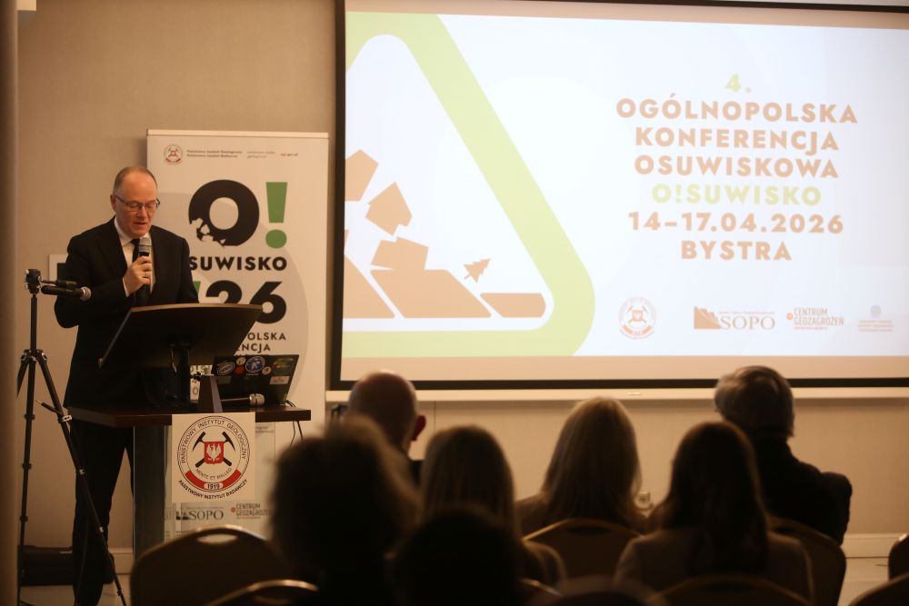 mężczyzna z mikrofonem w ręce podczas prelekcji, na tle ekranu