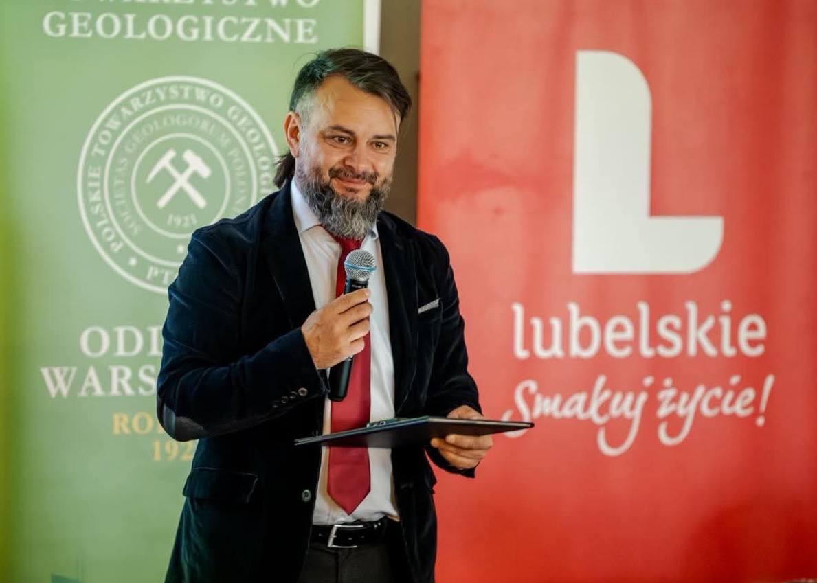 mężczyzna z mikrofonem w ręce podczas prelekcji, na tle ekranu