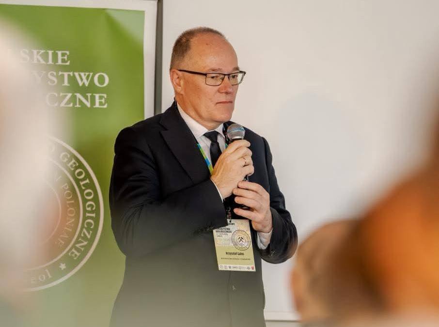 mężczyzna z mikrofonem w ręce podczas prelekcji, na tle ekranu