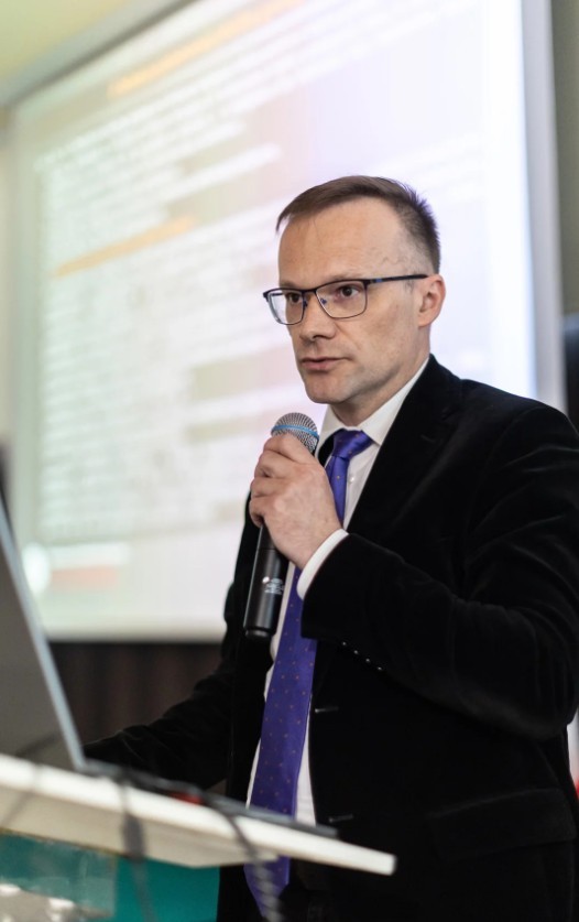 mężczyzna z mikrofonem w ręce podczas prelekcji, na tle ekranu