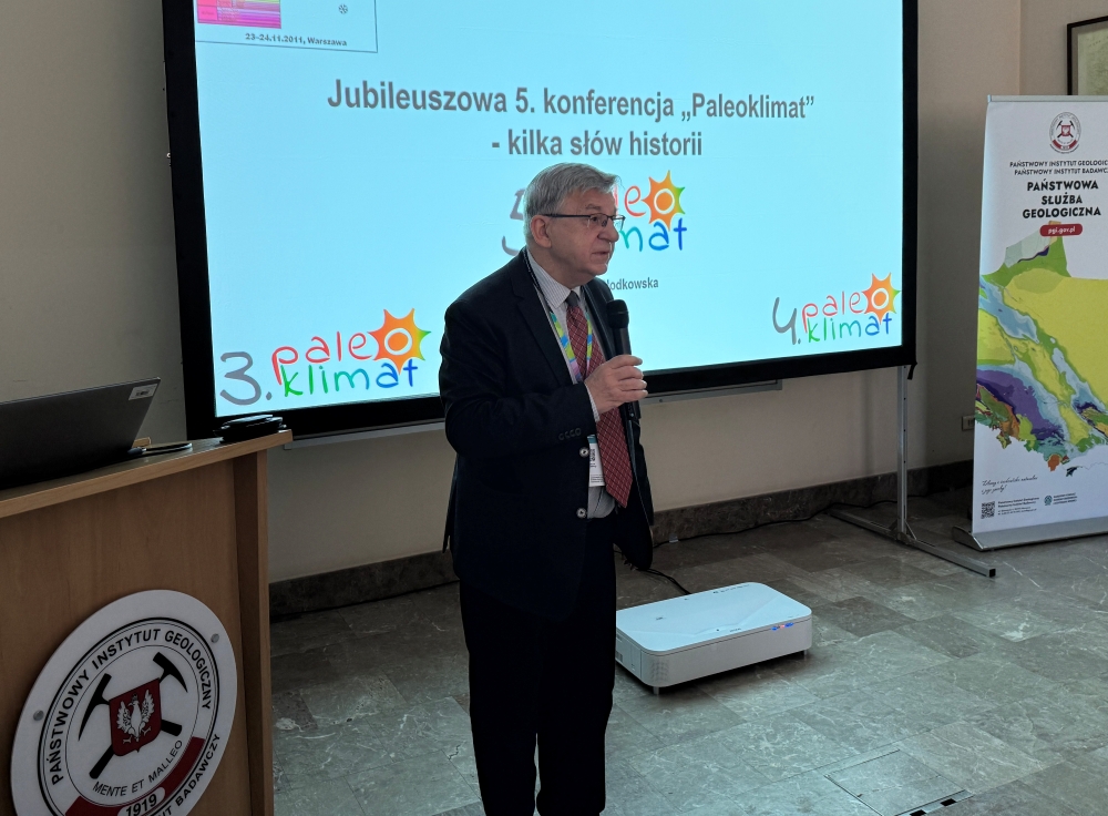 mężczyzna z mikrofonem w ręce podczas prelekcji, na tle ekranu