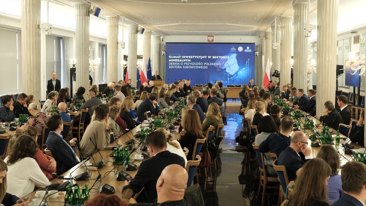 grupa osób siedząca na sali przy stole i prowadzących rozmowę ze sobą