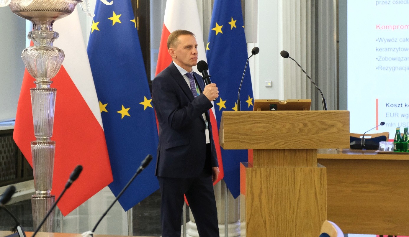 mężczyzna z mikrofonem w ręce podczas prelekcji, na tle ekranu