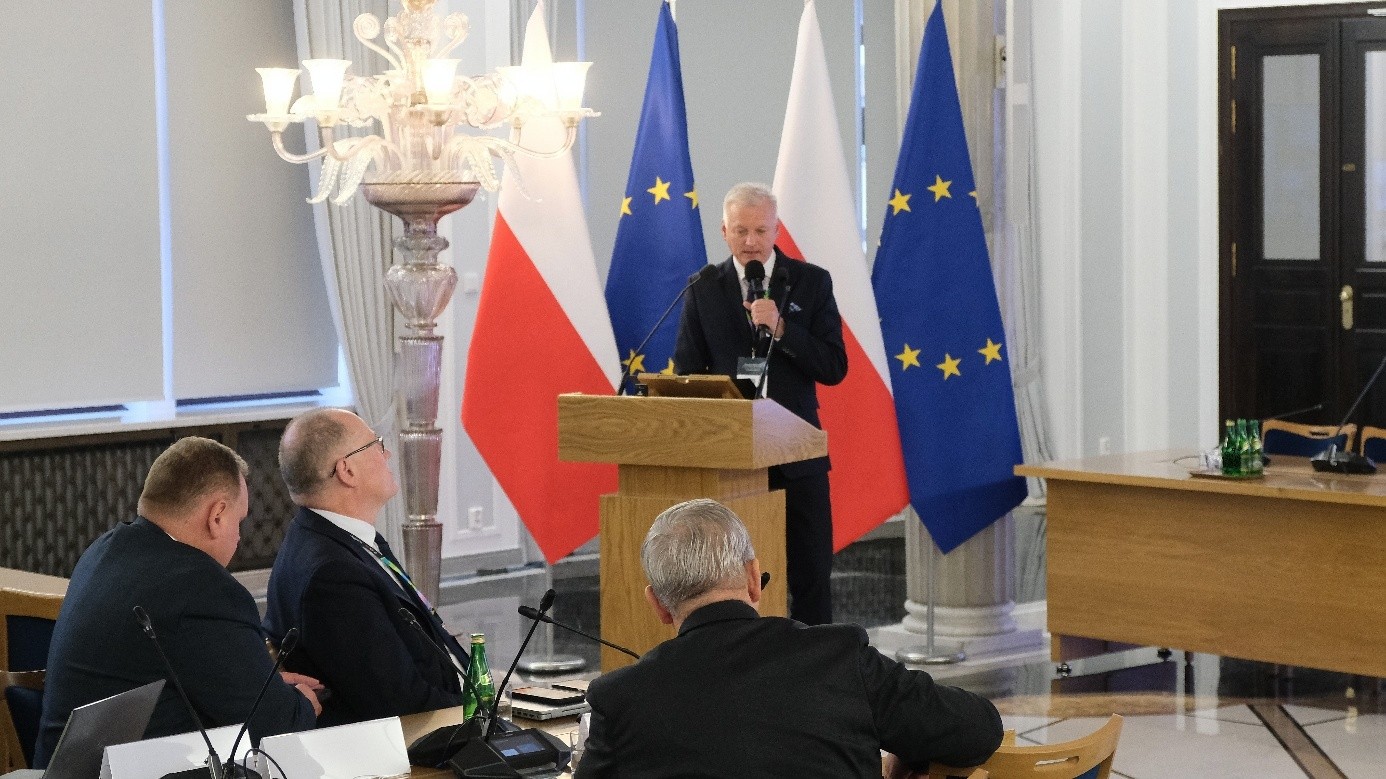 mężczyzna z mikrofonem w ręce podczas prelekcji, na tle ekranu