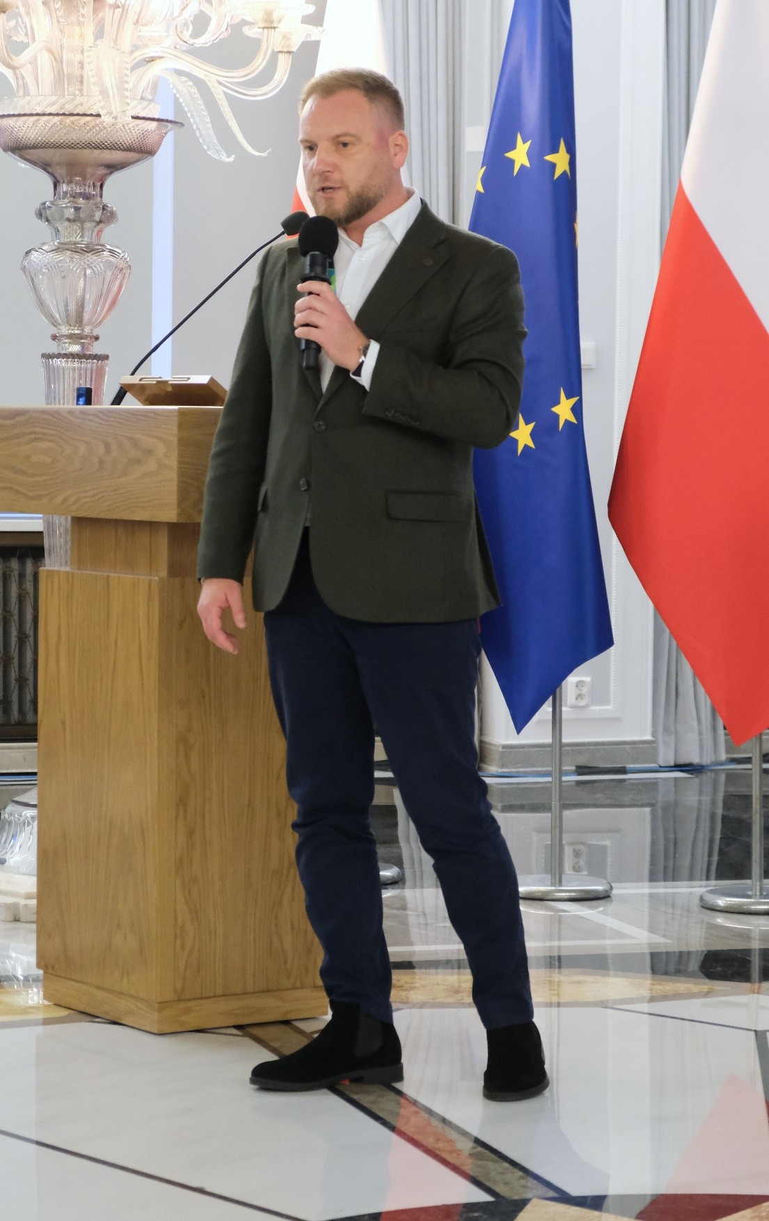 mężczyzna z mikrofonem w ręce podczas prelekcji, na tle ekranu