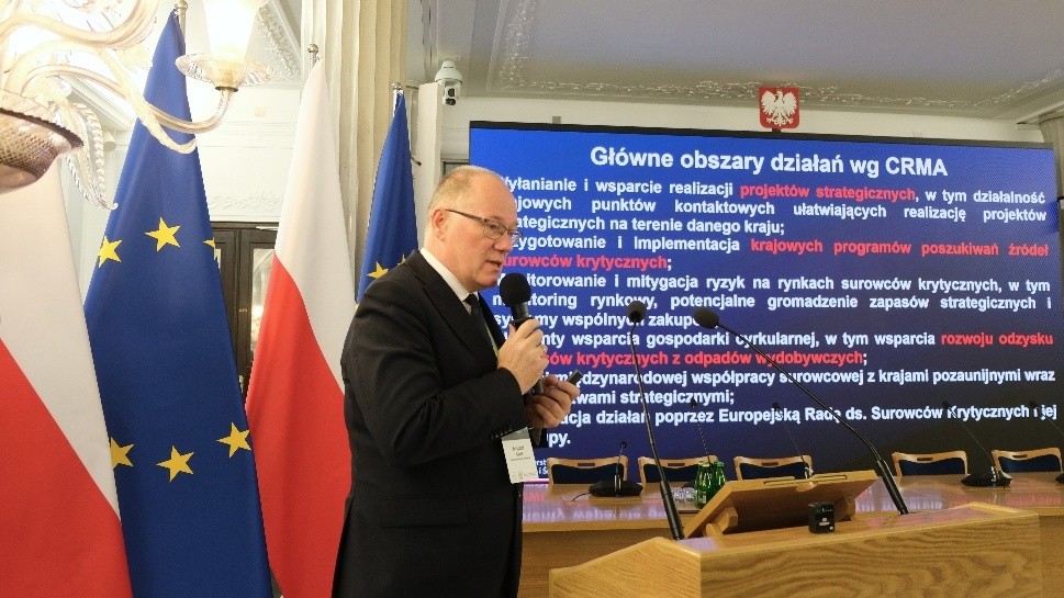 mężczyzna przemawia do siedzącej w pomieszczeniu publiczności