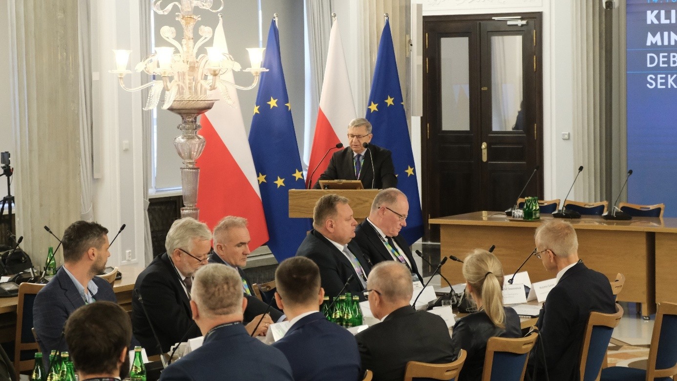 mężczyzna przemawia do siedzącej w pomieszczeniu publiczności