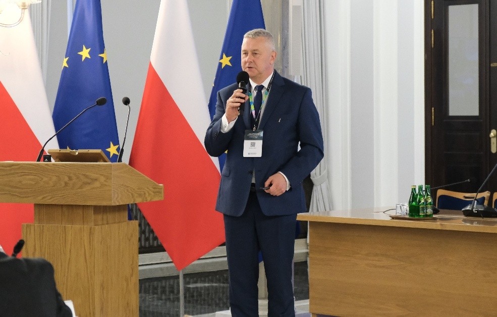 mężczyzna z mikrofonem w ręce podczas prelekcji, na tle ekranu