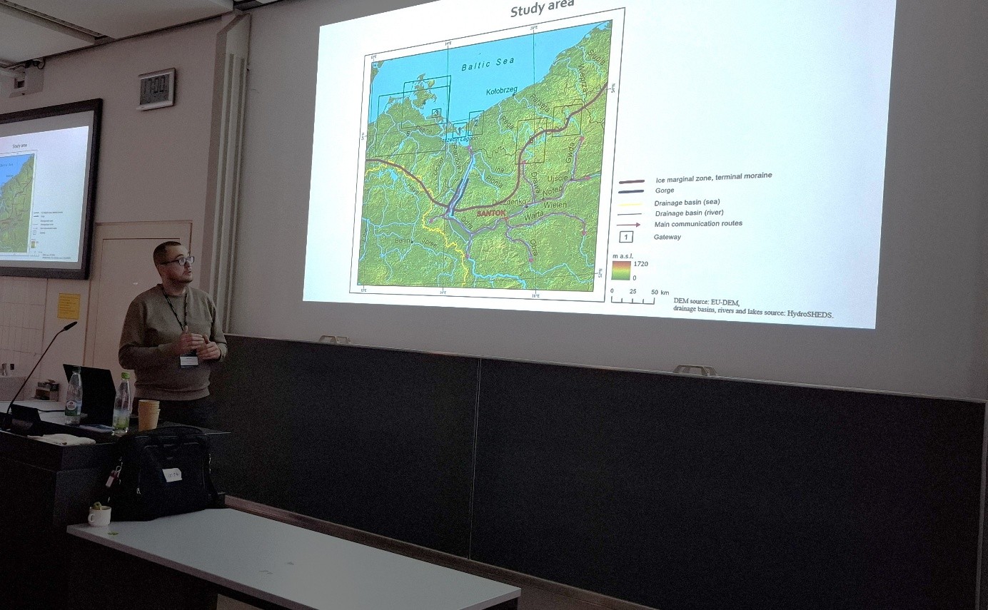 mężczyzna z mikrofonem w ręce podczas prelekcji, na tle ekranu