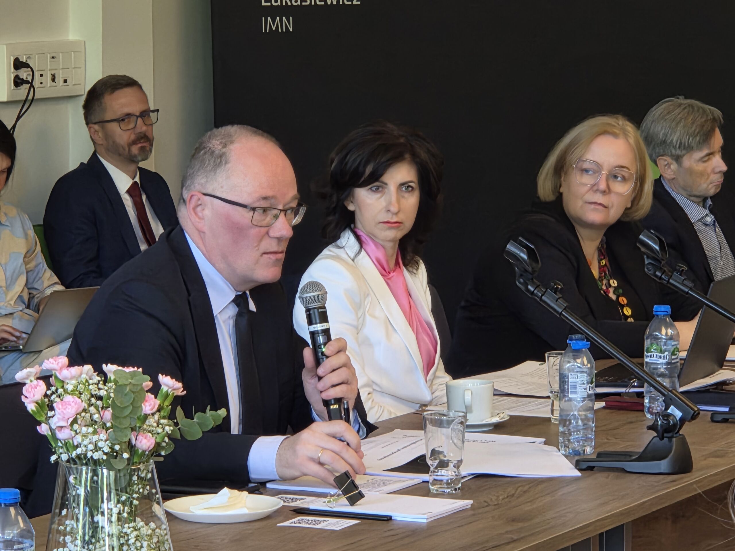 grupa osób siedząca na sali przy stole i prowadzących rozmowę ze sobą