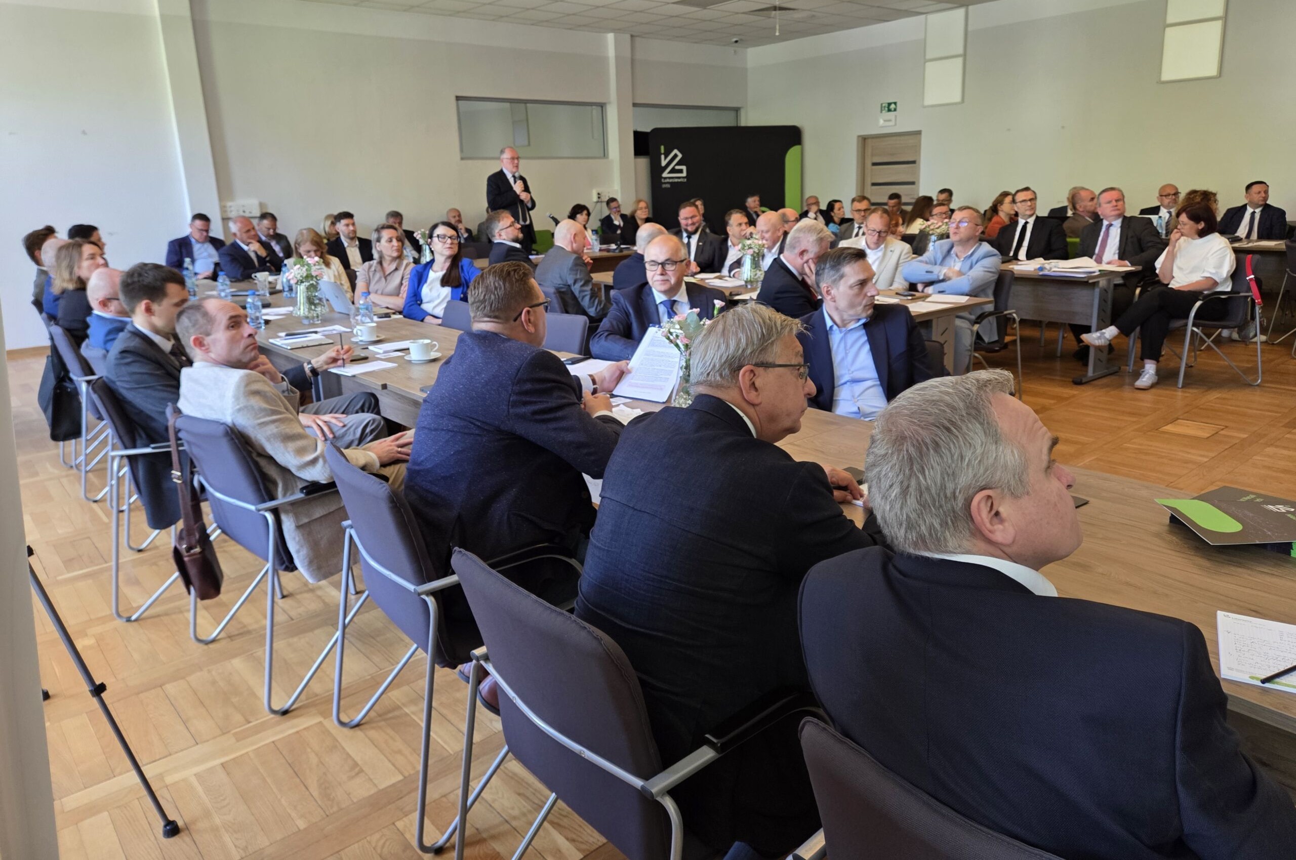 grupa osób siedząca na sali przy stole i prowadzących rozmowę ze sobą