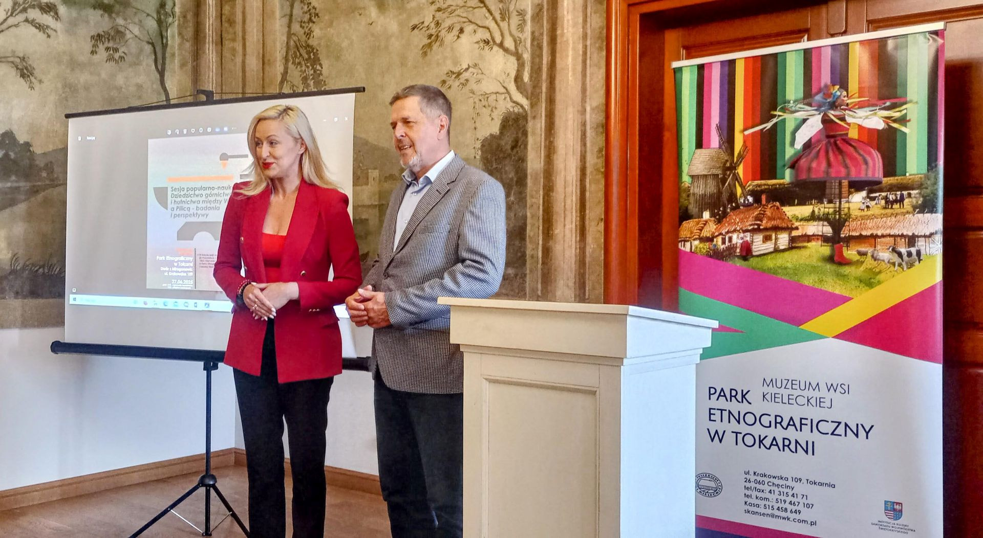 dwie osoby przemawiają do publiczności na sali