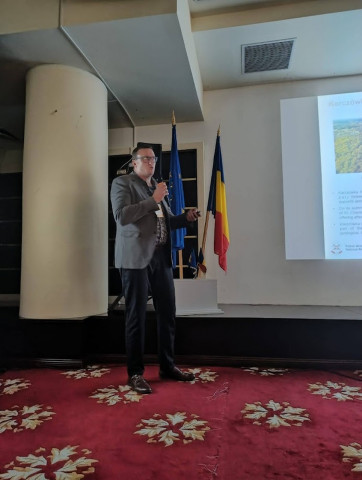 mężczyzna z mikrofonem w ręce podczas prelekcji, na tle ekranu